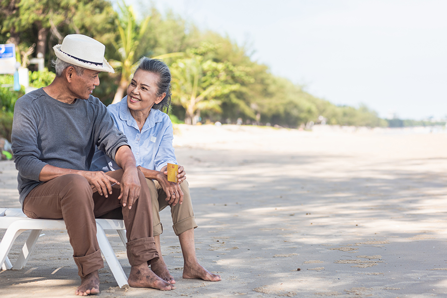 happy retired couple sitting on beach discussing life insurance in retirement